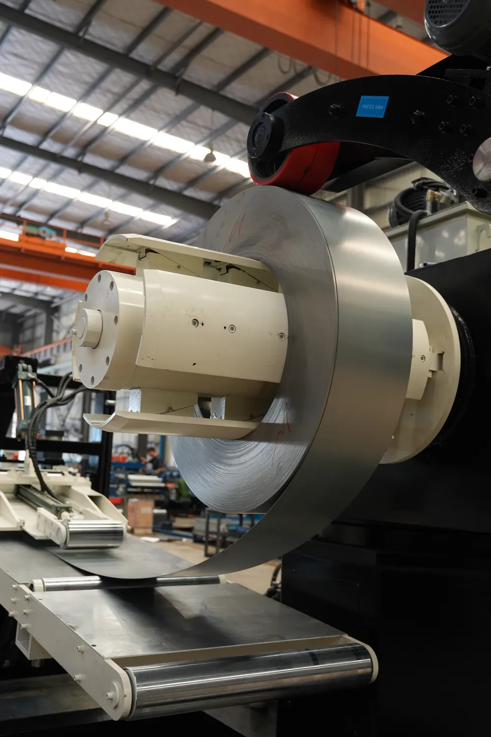 Site-visit photo of a steel coil on a decoiler mandrel with strip feeding across guide rollers