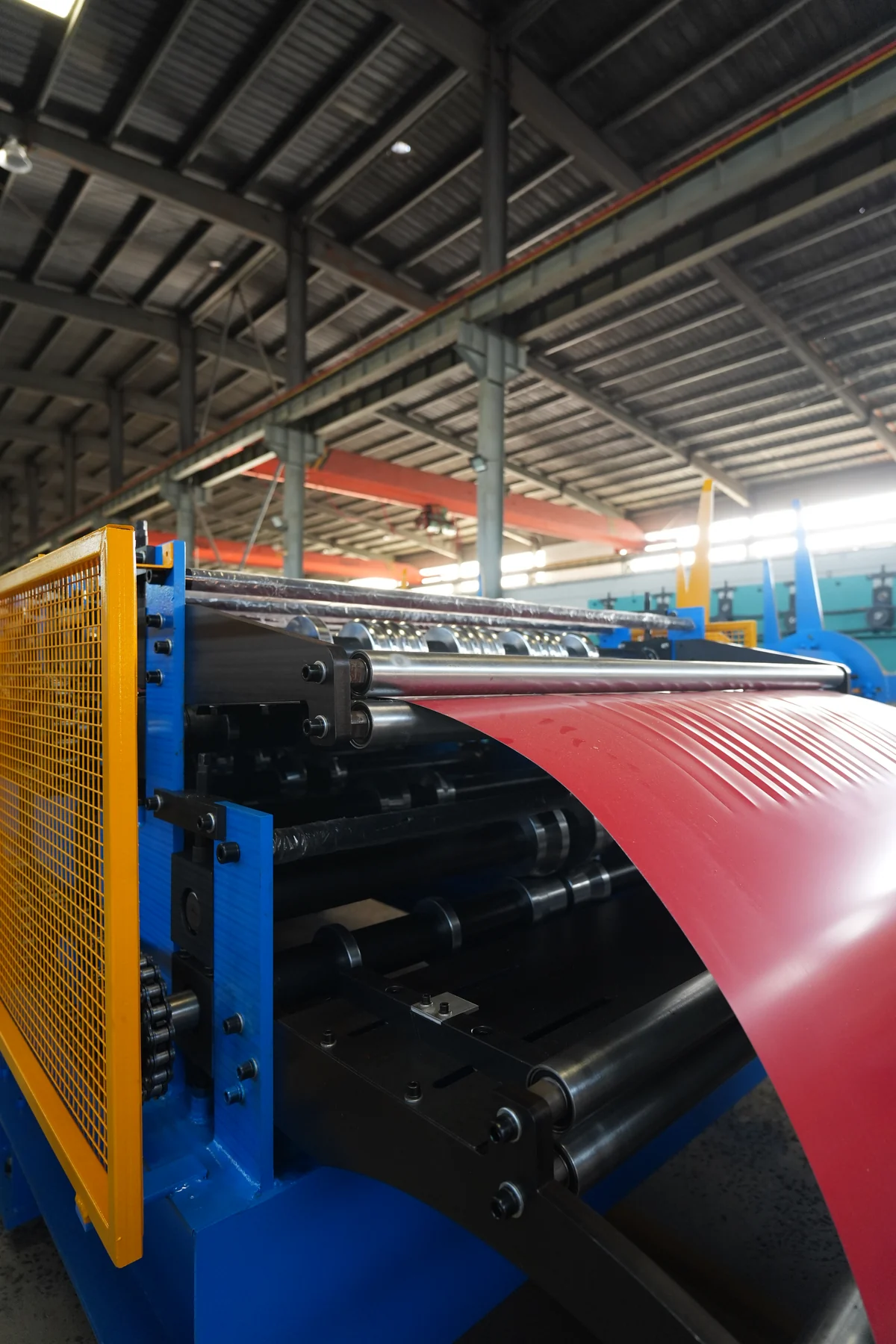Red finished-surface metal sheet at forming rollers in a workshop